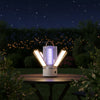 Rechargeable LED Mosquito Killer Lamp and Lantern illuminated at night on a table surrounded by greenery.