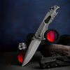 High Hardness Steel Folding Survival Pocket Knife resting on a surface with a dark background and red accents.