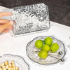 Hand holding System Storage container next to 6 Pc Flower-Shaped Snack Tray with green grapes and snacks.