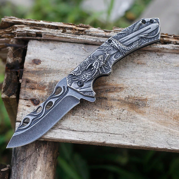 3D Embossed Dragon Folding Survival Knife resting on wooden surface, showcasing intricate handle design and sharp blade.