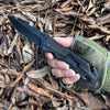 4-Function Portable Stainless Steel Survival Knife held in hand among fallen leaves.