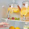 Glass Beverage Dispenser with Faucet pouring lemonade into a glass on a fridge shelf, showcasing refreshing beverage service.