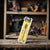 Hex Shank Flat Wood Drill Bit packaging displayed in a workshop with various tools in the background.