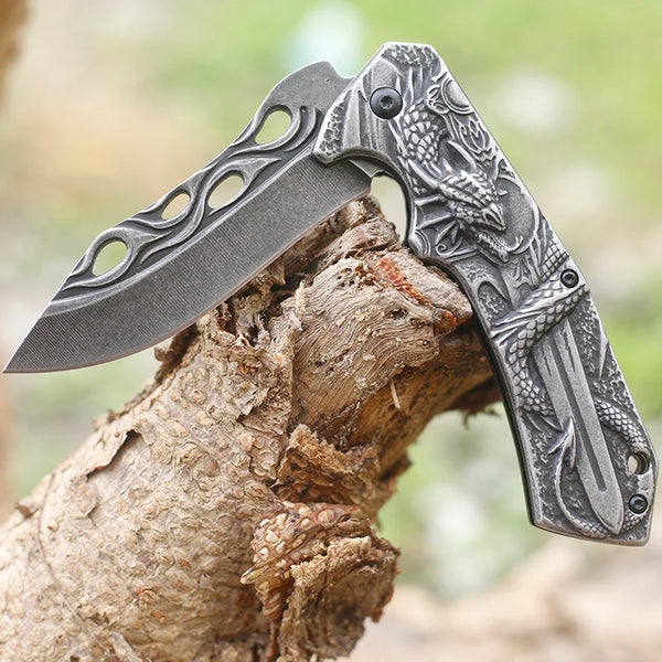 3D Embossed Dragon Folding Survival Knife resting on a tree log, showcasing its intricate design and sharp blade.