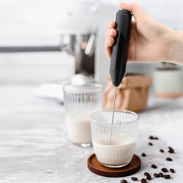Electric Handheld Milk Frother in use, creating creamy foam in a glass beside coffee beans.