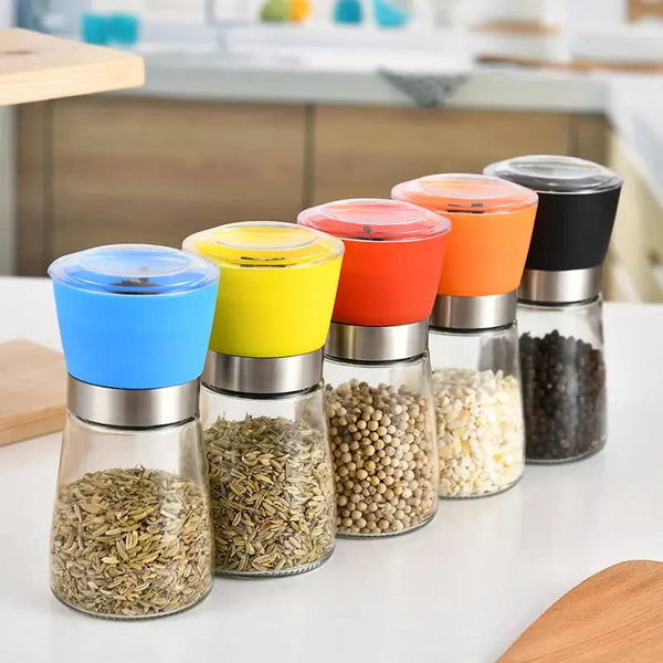 Colorful manual spice grinders on a kitchen table, including a Manual Stainless Steel Pepper & Salt Grinder Mill design.