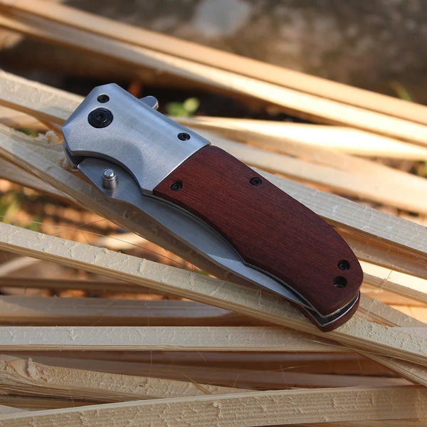 Wooden Handle Folding Tactical Pocket Knife resting on wooden sticks outdoors.