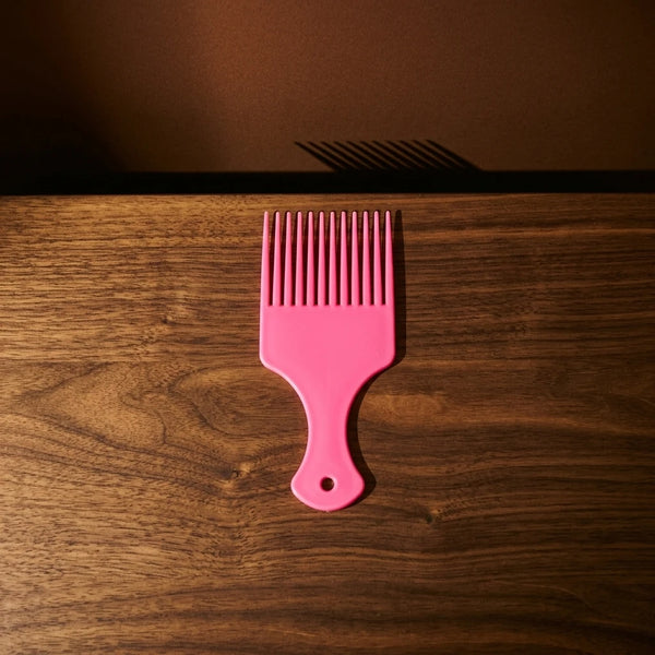 Wide-Tooth Hair Pick Comb in pink color on a wooden surface with a shadow.