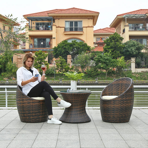 Woman enjoying a drink while relaxing in the Garden Lounge Wicker Furniture Set by a serene outdoor waterfront.