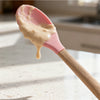 Silicone Cooking Spoon with Wooden Handle holding creamy mixture on a kitchen countertop.