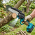 A user operates the 6-Inch Cordless Mini Lithium Electric Chainsaw to trim branches in a garden.