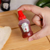 Hand holding a Mini 30ml Plastic Squeeze Bottles filled with ketchup on a wooden surface.