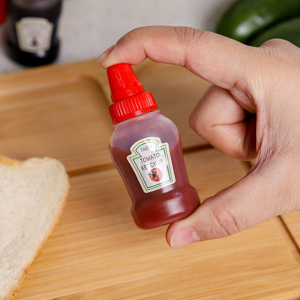 Hand holding a Mini 30ml Plastic Squeeze Bottles filled with ketchup on a wooden surface.