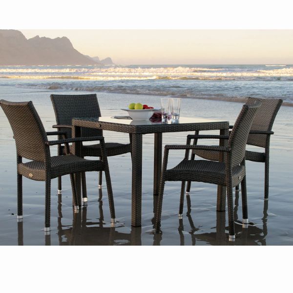 Rattan Patio Dinner Table Set on the beach with square glass top and four rattan dining chairs.