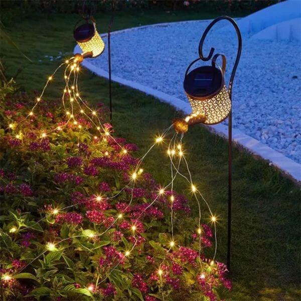 Solar-Powered Watering Can Garden Light illuminating flowers in a garden at night.