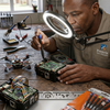 A technician using a magnifying lamp to repair electronics with a 6 Piece Triangle Head Precision Screwdriver Set on the table.