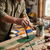 Person using a Professional 3 Inch Nylon Paint Brush to apply green paint on wood in a workshop.