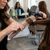 Stylist using a Round Styling Hair Brush to create smooth, voluminous hair while blow-drying in a salon.