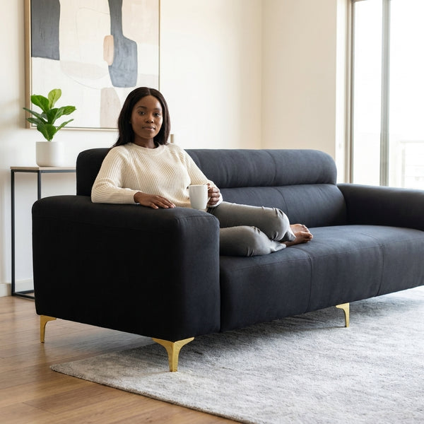 Modern Black 3-Seater Sofa with Gold Metal Legs in a stylish living room setting with a woman relaxing.