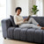 Modern Grey Upholstered 2-Seater Sofa with a woman relaxing and using a tablet in a bright living space.