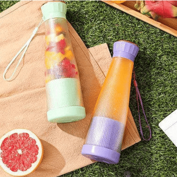 Smoothie Blender Cups in green and purple on a picnic blanket with fresh fruits for healthy blending on the go.