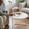 A person enjoying a cup of coffee at a Scandinavian Round Coffee Table in a modern living room setting.