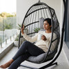 A woman relaxing in a Steel Frame Hanging Egg Chair on a balcony, enjoying a cup of coffee.