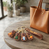 3D Silicone Capybara Keychain with Wrist Strap and brown tote bag on a wooden table.