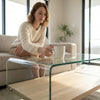 Woman enjoying coffee at a Tempered Glass Coffee Table with Oak Shelf in a modern living room.