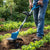 Person using a Cordless Lithium-Ion Rotating Tiller Grass Cutter in a garden, tilling soil and cutting grass.