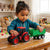 Child playing with a Plastic Farm Tractor Toy with Detachable Green Trailer on a table.