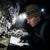 A person using a Head LED Light while examining a map in a dark cave environment.