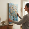 A woman hanging the Vertical Golden Tree Canvas Wall Art on a wall, showcasing its elegant design and metallic accents.