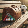 Football Silicone Keychain attached to a brown duffle bag with a soccer ball in the background.