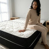 A woman sitting on the 1.5M Medium Firm Support Foam Mattress in a cozy bedroom setting.
