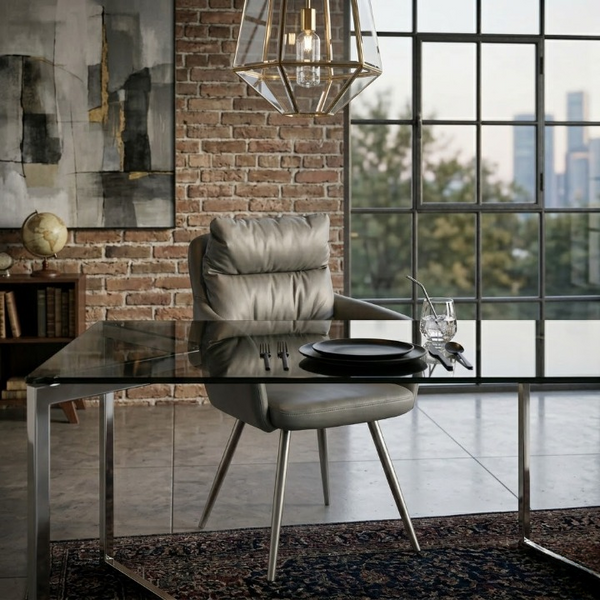Elara Modern Armchair at a stylish dining table with elegant glass top and rustic brick wall backdrop.