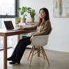 A woman sitting in an Eiffel Armchair with Wooden Legs at a desk, working on a laptop in a modern room.