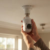 A person installing the Wireless Wi-Fi Light Bulb Security Camera in a ceiling socket.