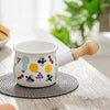 Small Enamel Milk and Butter Warming Pot with colorful design and wooden handle on a kitchen table.