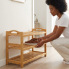 Standing Bamboo Shoe Rack 3-Tier Organizer with a woman placing shoes on a natural bamboo shelf in an entryway.
