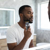 A man using a Rechargeable Hair Clipper Grooming Kit in front of a bathroom mirror for beard trimming.