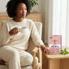 Woman enjoying Womb Care Herbal Tea - Women’s Wellness & Herbal Infusion in a cozy setting with packaging displayed.