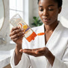 Vitamin C Body Oil Gel Skin Repair being poured into a woman's hand in a bathroom setting.