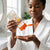 Vitamin C Body Oil Gel Skin Repair being poured into a woman's hand in a bathroom setting.