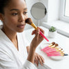 Woman applying makeup with 8pcs Candy Color Portable Travel Makeup Brush Set in a bright setting.