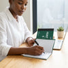 A6 Feint Ruled Duplicate Book Pack being used by a woman writing notes at a desk with a laptop.