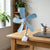 5 Blade Cooling Plastic Handheld Fan providing airflow on a desk with plants and a laptop in the background.