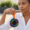Woman holding a Waterproof IPX5 Portable Speaker with vibrant lights, suitable for outdoor use.