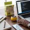 M3 Macaron Mini Wireless Speaker on a desk next to a laptop and phone, showcasing its portable design.