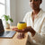 M3 Macaron Mini Wireless Speaker being held by a woman next to a laptop on a wooden desk.